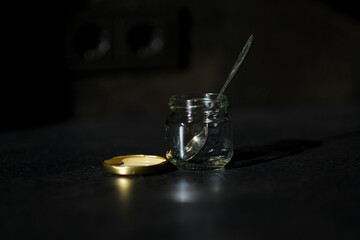 An empty jar is open. There is a teaspoon in the jar. The lid is next to the jar. A blank background.