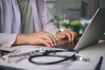 Male physician using computer for online patient consultation, managing digital health records, medical diagnosis on desk with stethoscope, representing telehealth and modern healthcare services.