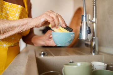 Midsection of senior woman scrubbing bowl with sponge in kitchen sink during household chores at home