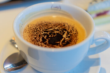 Close up of a white cup of cappuccino or espresso macchiato with a cocoa powder pattern on the foam, scene of breakfast or coffee break in a cafe, concept of coffee culture,