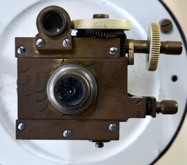 The lens of an optical instrument.
Close-up of the round eye of an old scientific instrument with adjustment wheels.