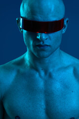A striking portrait of a man with a futuristic look, featuring a bald head and sunglasses, illuminated in vibrant blue light. Emphasizing a modern aesthetic.