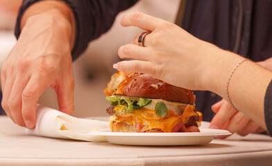 Two people at a food festival in Karlín Square, Prague, sharing a freshly prepared gourmet burger with melted cheese and vegetables, highlighting a social dining moment.