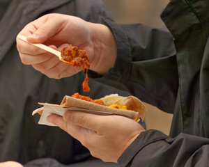Close-up of a visitor eating pulled meat with vegetables on flatbread using a wooden fork at a food festival in Karlin, Prague, lively street food atmosphere.