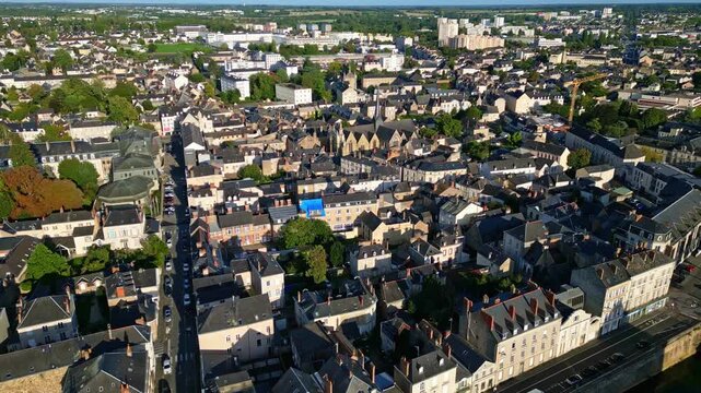 Drone advances above Laval, showing Mayenne river, Saint-Vénérand Church, main street, and city buildings in sunlight.