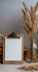 Rustic wooden clipboard with blank white paper sits next to dried pampas grass bouquet
