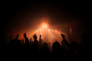 Fototapeta premium Silhouette of a congregation with hands raised in fervent worship towards a radiant cross, bathed in dramatic light and atmospheric smoke