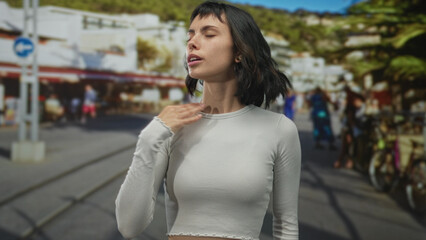 Woman fans hand at face under bright sunlight on a crowded urban street near bicycle rack and summer market stalls; relief.