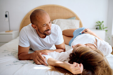 Happy diverse couple relaxing in bedroom, sharing an intimate moment and enjoying their time together