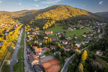 Aerial view of Silesian Beskids mountain town with river, tennis courts, and green hills at sunset, southern Poland