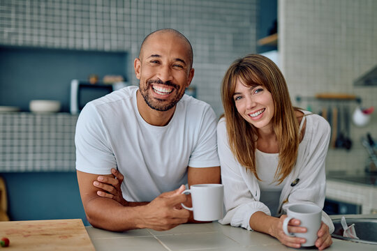 Happy diverse couple smiling, drinking coffee together in their kitchen. Sharing a relaxing morning lifestyle moment