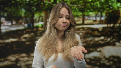 Obraz premium Woman displays rubbing fingertips and presenting open palm gesture while asking for money in green park under tree canopies; pleading need.