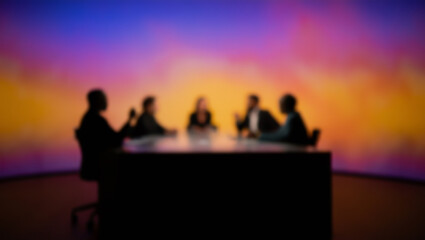 Fototapeta premium A blurred image of a group of people sitting at a table, engaged in a discussion or interview in a television studio, with a colorful, abstract background creating a dynamic atmosphere