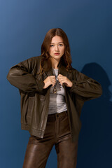 Young woman displays chic autumn style in brown leather against a blue backdrop