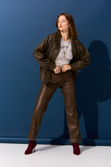 Young woman models autumn fashion in a brown leather outfit with a blue background
