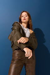 Young woman showcases stylish brown leather outfit in blue studio setting during autumn