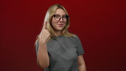 Obraz premium Woman smiling and gesturing on an isolated red background, creating a joyful, uplifting moment with blonde hair and glasses.