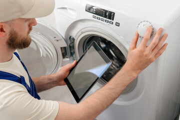Repairman checks washing machine settings using tablet at home