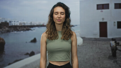 Woman with closed eyes and visible face at seaside promenade by rocky coast; quiet contemplation serenity.
