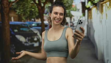 Young hispanic woman holds smartphone at arm extension on urban street lined with parked cars; happiness.