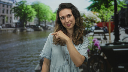 Fototapeta premium Woman finger pointing to canal on street in amsterdam wearing a blue dress and smiling on a bright sunny day; curiosity.
