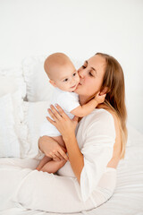 mother and baby hugging and kissing on the bed at home, maternal love and care, mother and child
