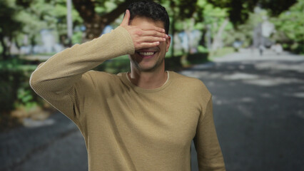 Man places hand to cover eyes in outdoor scene with hispanic young smiling face at a park by a guy.