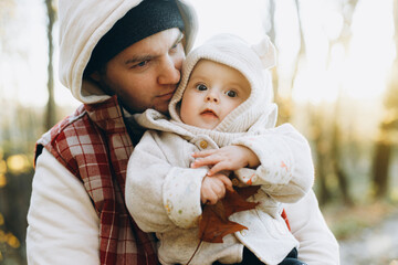 Obraz premium Happy father hugging and kissing cute baby son in soft evening light in autumn woods. Fatherhood. Stylish man with adorable child in cozy warm sweaters embracing in fall park