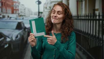 Woman smiling on city street holding learner sign confidently exhibits her excitement and readiness for driving with urban background.