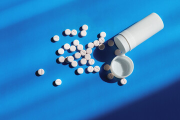 Tablets spilled from a packaging tube on a light blue background in bright sunlight close-up.
