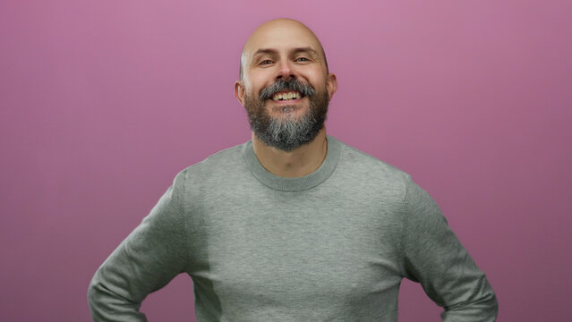 Bearded man with bald head stands confidently against isolated pink background conveying positive and approachable vibe