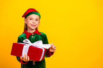 Festive young elf in green costume holding red wrapped gift, cheerful holiday concept against vibrant yellow background