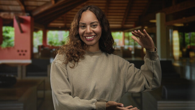 Woman smiling with eyes closed and gesturing with open hands in a hotel lobby building; welcoming joy.