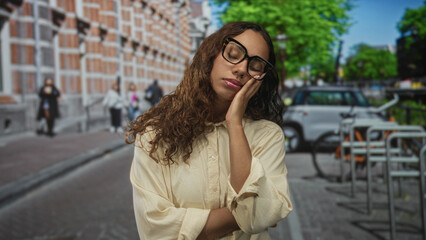 Fototapeta premium Woman with hand on cheek and closed eyes touching face while standing on street near parked car and bike rack; sleepy solitude.