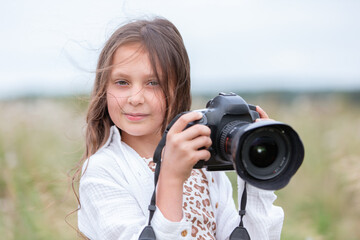 Young girl enjoys outdoor photography while holding a camera in a grassy field on a cloudy day