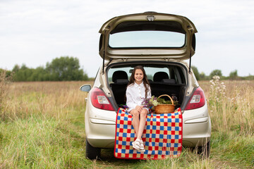 Girl enjoys a picnic by her car in a grassy field on a calm day