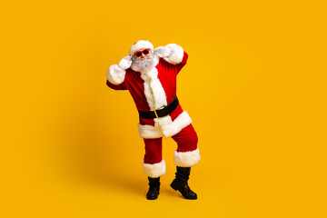 Santa Claus dancing in a festive pose wearing sunglass on a bright yellow background celebrating the Christmas season