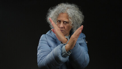 Woman with grey hair in blue coat gesturing on black background with a serious expression,...