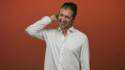Man with hand on neck showing neckache in a studio setting against an orange backdrop with a pained...