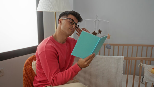 Young man reading in a cozy bedroom nursery with baby crib and soft lighting, embodying a serene and thoughtful moment indoors. - Powered by Adobe