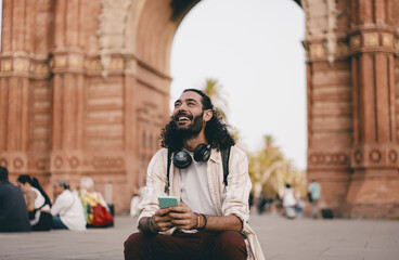 Obraz premium Young man laughs while holding phone outdoors, expressing emotional connection, mobile joy and spontaneous reaction in digital freelance lifestyle.