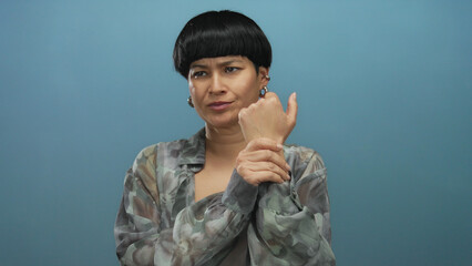 Young woman experiencing wrist pain against a blue background holds her wrist with a concerned expression emphasizing discomfort and medical condition.