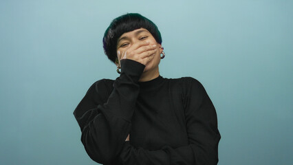 Woman laughing covering mouth isolated against blue background wearing black sweater featuring...