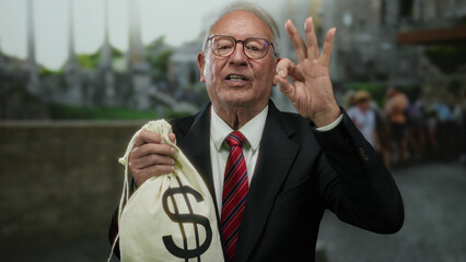 Senior man in suit showing ok gesture holding money bag in ancient roman ruins, implying corruption...