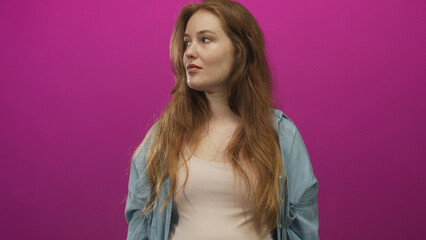 Woman with long red hair in denim shirt turns head to the side in magenta studio; calm meditative reflection.