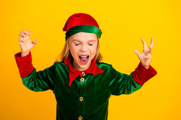 Excited girl in green elf costume expressing playful emotions on a vibrant yellow background, portraying festive holiday cheer