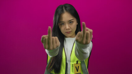 Woman in reflective vest gestures with both middle fingers against a vibrant pink wall, expressing...