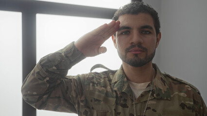 Man in military uniform salutes in a sunlit living room beside a large window while dog tags hang...