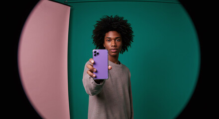 Confident young man showcasing sleek purple smartphone with modern design and vibrant color against a stylish studio backdrop for tech enthusiasts