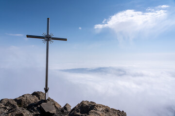 Lonely cross standing on rocky peak above sky full of clouds